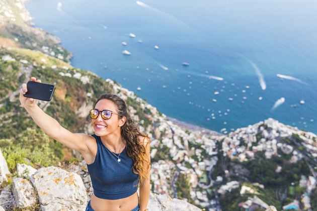 A young woman is taking a selfie. Positano village in the background