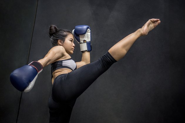 Young Asian woman boxer with blue boxing gloves kicking in the exercise gym