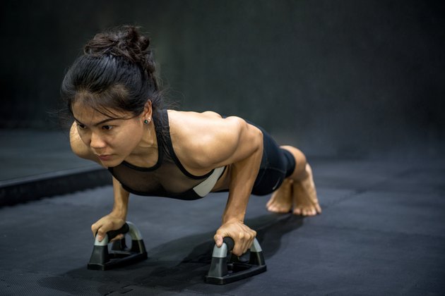 Young Asian athlete woman doing push up with push-up bars on the floor