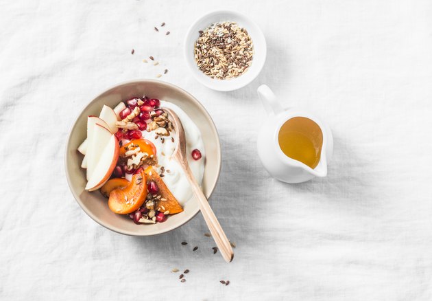 Full fruit and greek yogurt breakfast bowl. Persimmon, apple, walnuts, pomegranates and natural yogurt. Healthy food concept on light background, top view