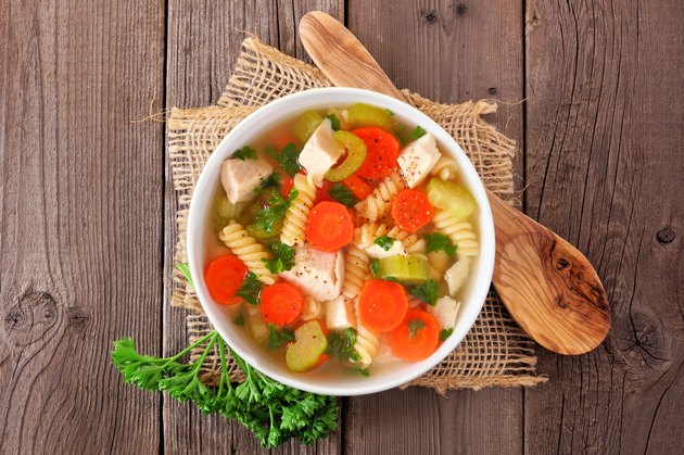 Homemade chicken noodle soup with vegetables, top view on a wood background