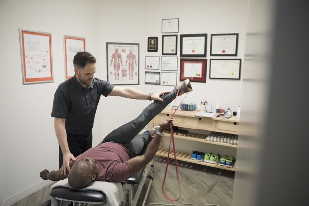 Male physiotherapist helping client stretching with resistance band in office