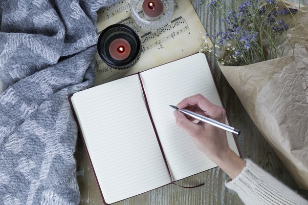 woman's hand writing in notebook near candles and flowers