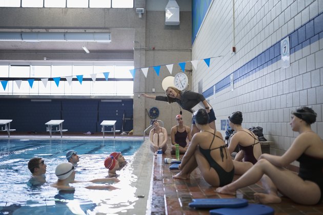 女教练在游泳池练习时向游泳者讲解泳姿