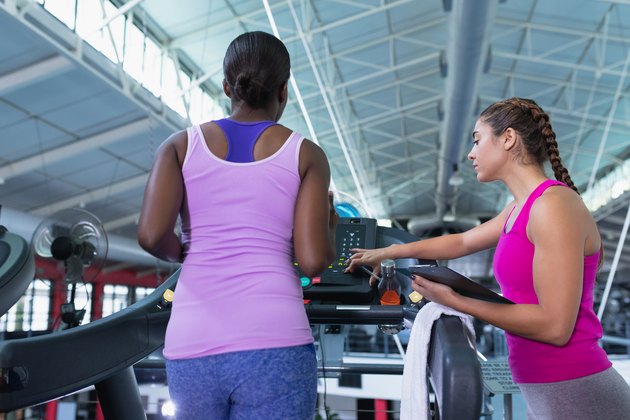 Female trainer assisting woman to work out on treadmill