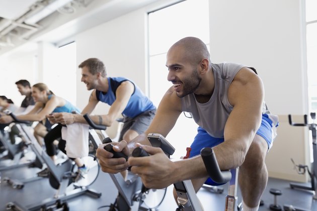 微笑的男人享受健身班固定自行车健身房