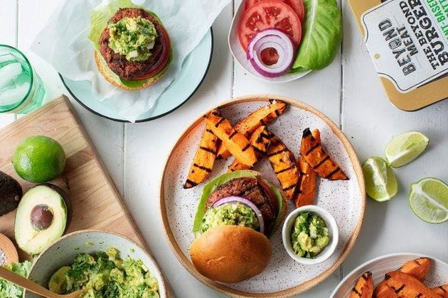lifestyle shot of food spread with Beyond Meat burgers, sweet potato fries, toppings and guacamole