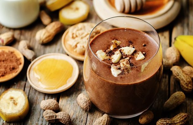 Smoothie au beurre d'arachide-banane-cacao sur la table avec du miel et des arachides