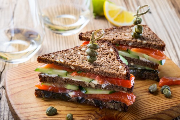 在黑麦面包的自创三文鱼俱乐部三明治用黄瓜和嫩煎的菠菜和安全与鸡尾酒棍子