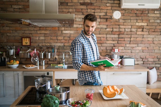 Jeune homme dans la cuisine essayant de préparer le déjeuner à partir d'un livre de cuisine.
