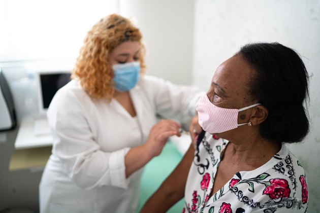 护士戴蓝色口罩给戴粉色口罩的病人注射疫苗