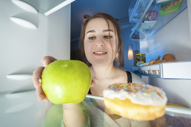 Portrait from inside the fridge of woman taking apple