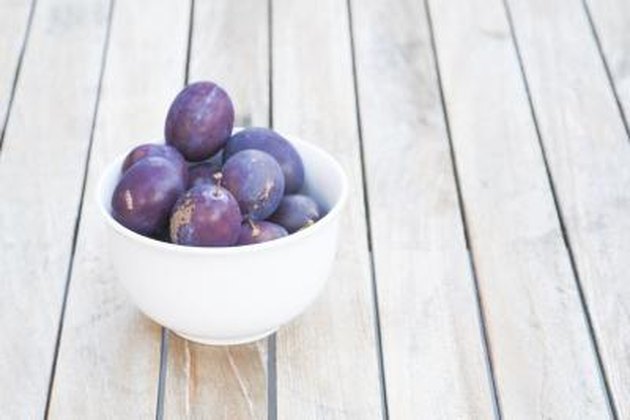 plums in white bowl on wood