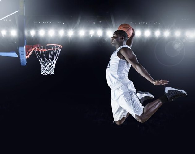 Composite image of basketball player scoring a slam dunk in a professional basketball game.