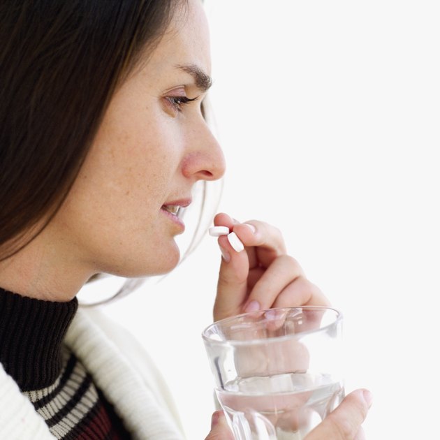 Side profile of a young woman taking a pill and holding a glass of water
