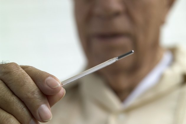 Man looking at thermometer, close-up, focus on hand and thermometer
