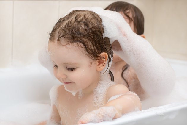 Two adorable little girls taking a bath with soap suds
