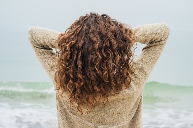 在海边穿着一件毛线衫的深棕色卷发女人
