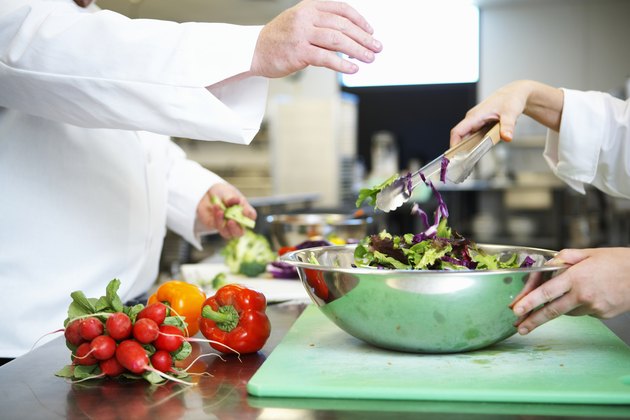 Chefs preparing salad in kitchen, mid section