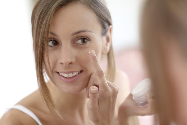 Brunette woman applying cream on face