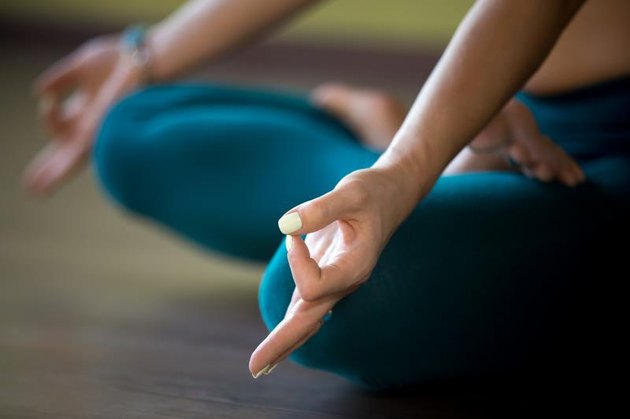 Sporty beautiful woman in sportswear working out indoors, sitting cross-legged in Padmasana, Lotus posture, asana for meditation, breathing exercises, close-up, focus on fingers in Jnana mudra