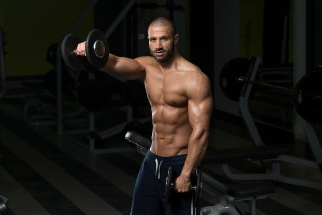 Muscular Young Man Doing Heavy Weight Exercise For Shoulders In Gym