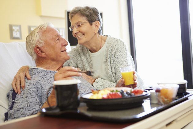 Senior Couple In Hospital Room As Male Patient Has Lunch