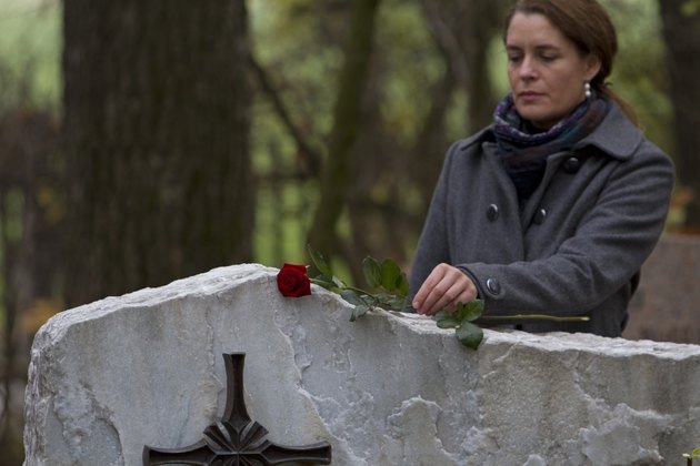 Mature woman placing red rose on gravestone in cemetery