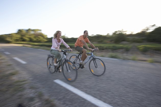 Woman and man riding bicycles on country road, focus on cyclists