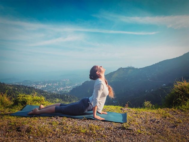 Yoga outdoors - woman practices Ashtanga Vinyasa yoga Surya Namaskar Sun Salutation asana Urdhva Mukha Svanasana - upward facing dog pose in mountains in the morning. Vintage retro effect filtered hipster style image.