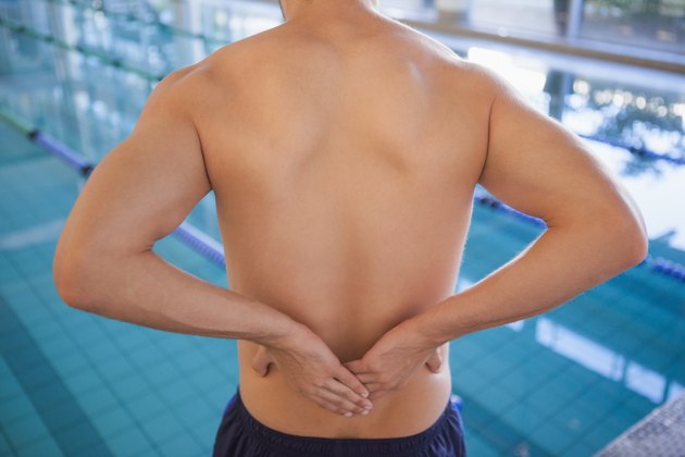 Fit swimmer touching his back by the pool