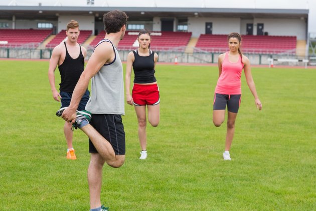 People stretching leg on grass against the stadium