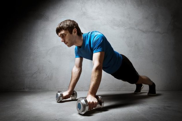 Man pushing up from the dumbbells on empty gray wall backdrop