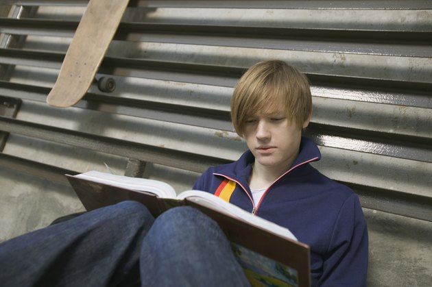 Teenage boy reading book outdoors
