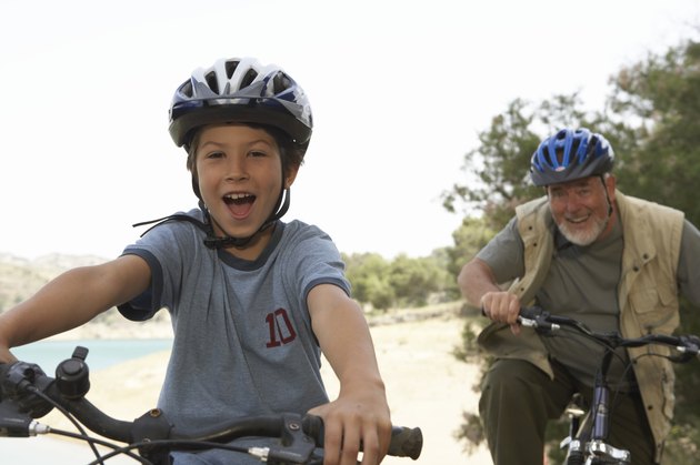 Grandson (5-7) and grandfather riding bikes, portrait (focus on boy)