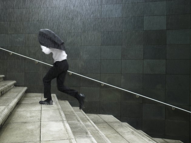 Businessman running up steps, sheltering under jacket, side view