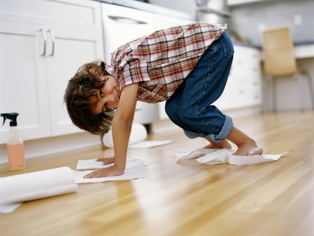 Boy (5-7) polishing floor with paper towel under hands and feet