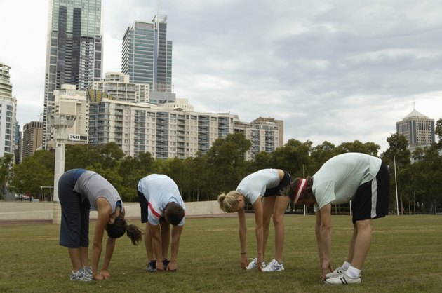 Young men and women stretching touching toes in park