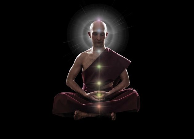 buddhist monk in meditation pose with colorful Chakras over black background