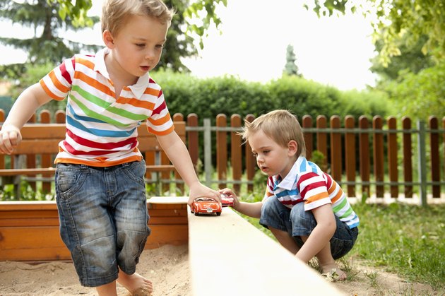 Twin brothers playing in sandpit with toy cars