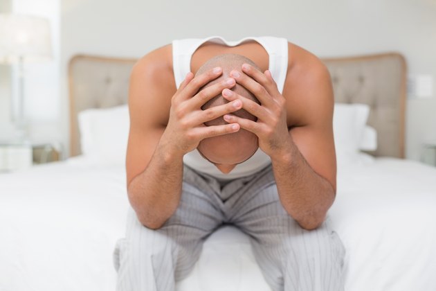 Thoughtful bald man with head in hands on bed