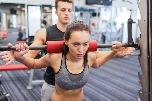 man and woman with barbell flexing muscles in gym
