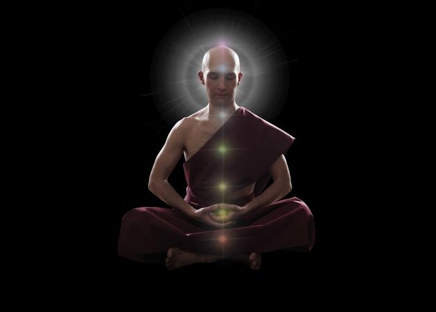 buddhist monk in meditation pose with colorful Chakras over black background