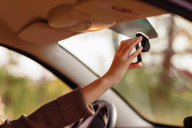 the girl in the car adjusts the rear view mirror