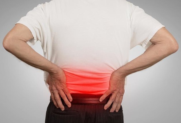rear view old man grandpa holding his painful lower back colored in red with hands isolated on gray background. Human health problems .