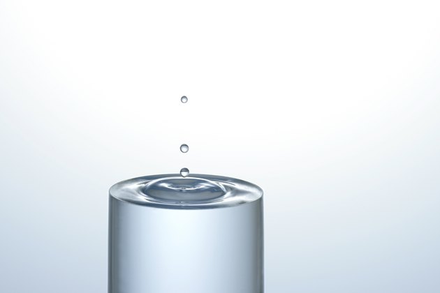 Water dropping onto a full glass of water, creating concentric circles on the surface