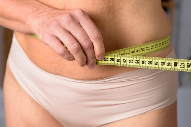 middle aged woman measuring her waist