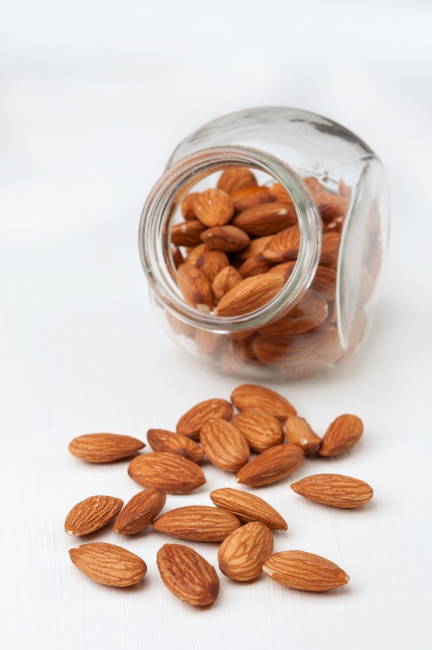 Almond nuts in a glass jar on white wooden background.