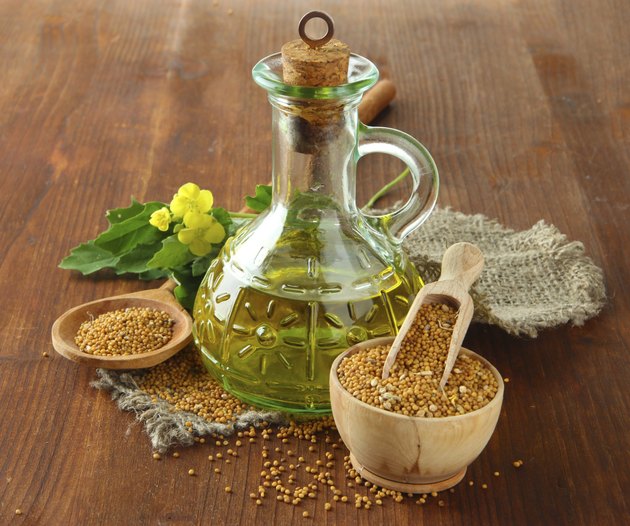 Jar of oil and mustard seeds on wooden background