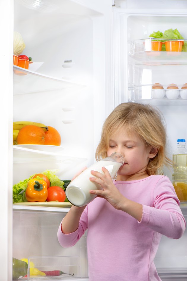 Little cute girl drinking milk near open fridge